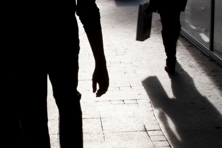 Blurry silhouette and shadow of a woman carrying a bag and a man following her, in the city street in the night